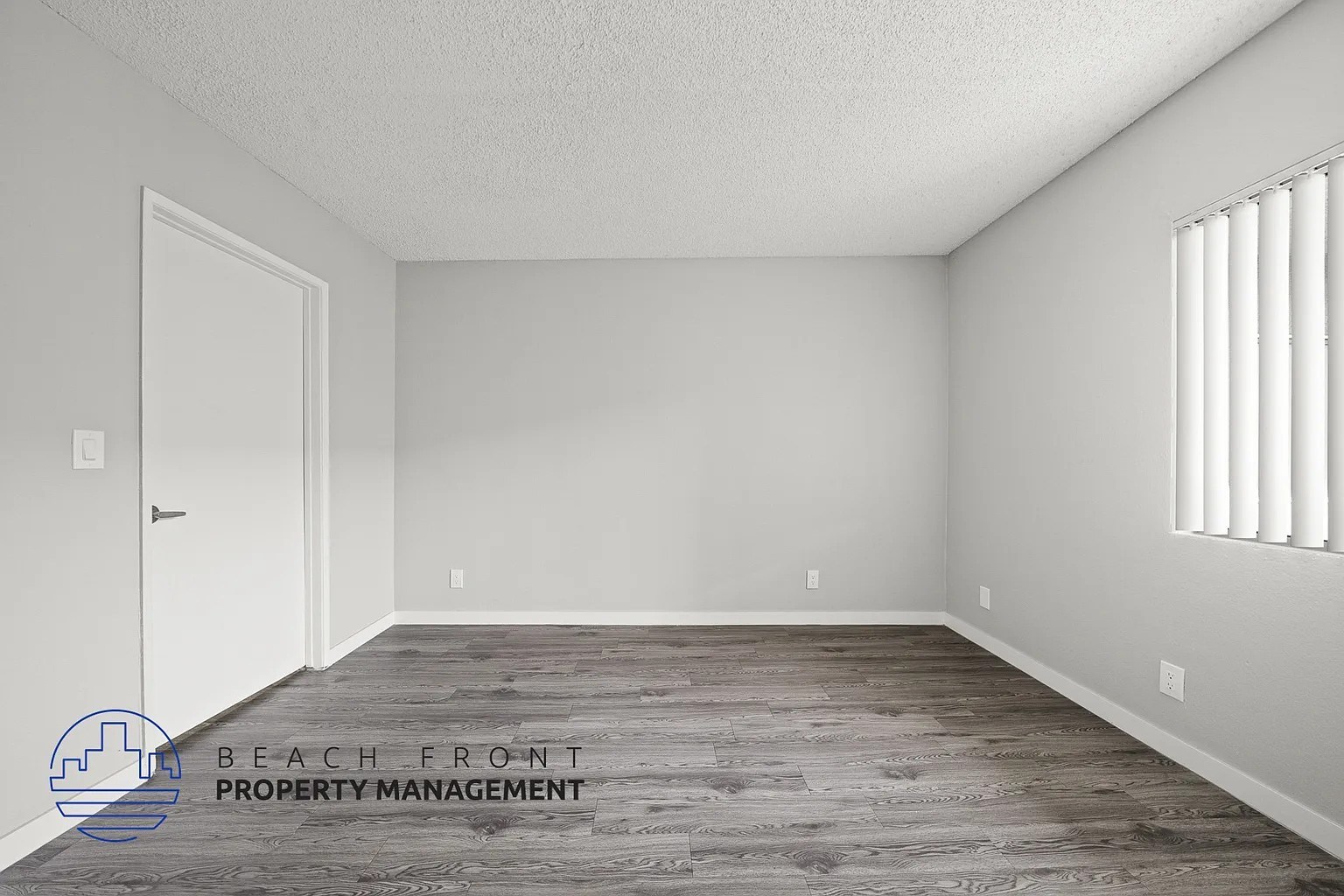 A room with a wooden floor and a window with blinds.